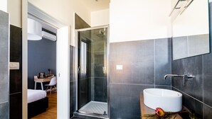 Casa de banho moderna com chuveiro envolto em vidro, pia branca e toucador de madeira.