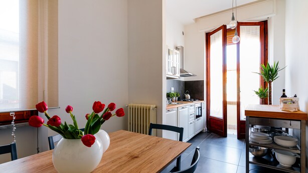 Uma cozinha moderna com armários brancos, uma mesa de jantar de madeira e um vaso de tulipas vermelhas.