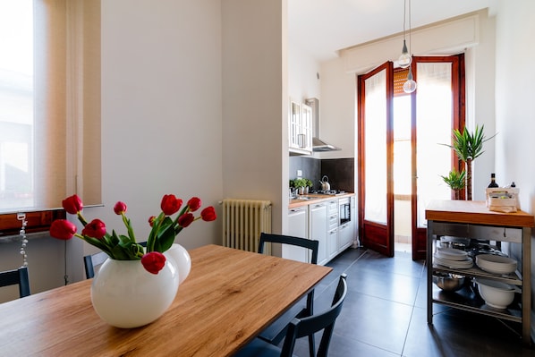 Una cocina moderna con armarios blancos, una mesa de comedor de madera y un jarrón con tulipanes rojos.