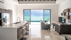 A modern kitchen with a large island, a dining area with a sofa, and a view of the ocean through large sliding doors. - SUMMER RATE Modern Beachfront 5bed - 5bath with incredible view (providenciales)