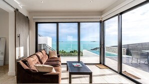 A modern living room with a large sliding glass door leading to a balcony with a pool and ocean view. - SUMMER RATE Modern Beachfront 5bed - 5bath with incredible view (providenciales)