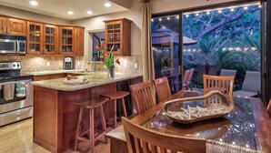 A kitchen with wooden cabinets, a stainless steel oven, and a dining area with a glass table and wooden chairs. - #1 GUEST FAVORITE for Napili & Kapalua Bays ! (Lahaina)