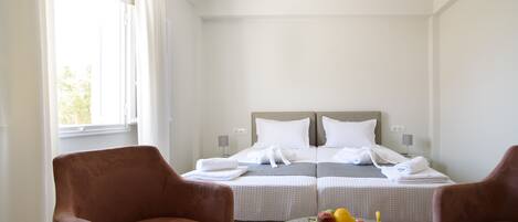 A hotel room with two beds, a round table with fruit and a book, and two chairs.