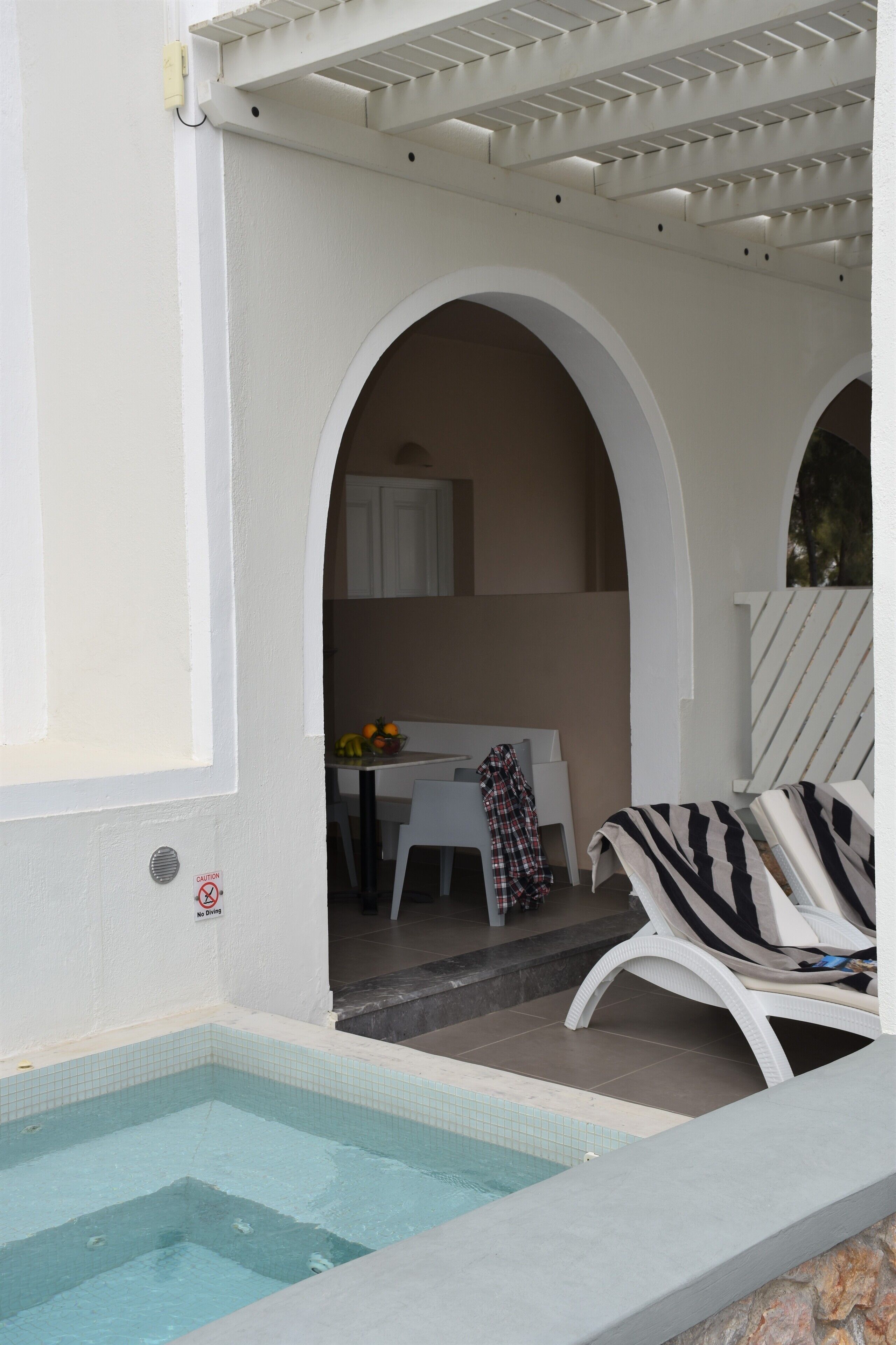 Area piscina con pavimento piastrellato, una poltrona da relax e un tavolo con frutta.