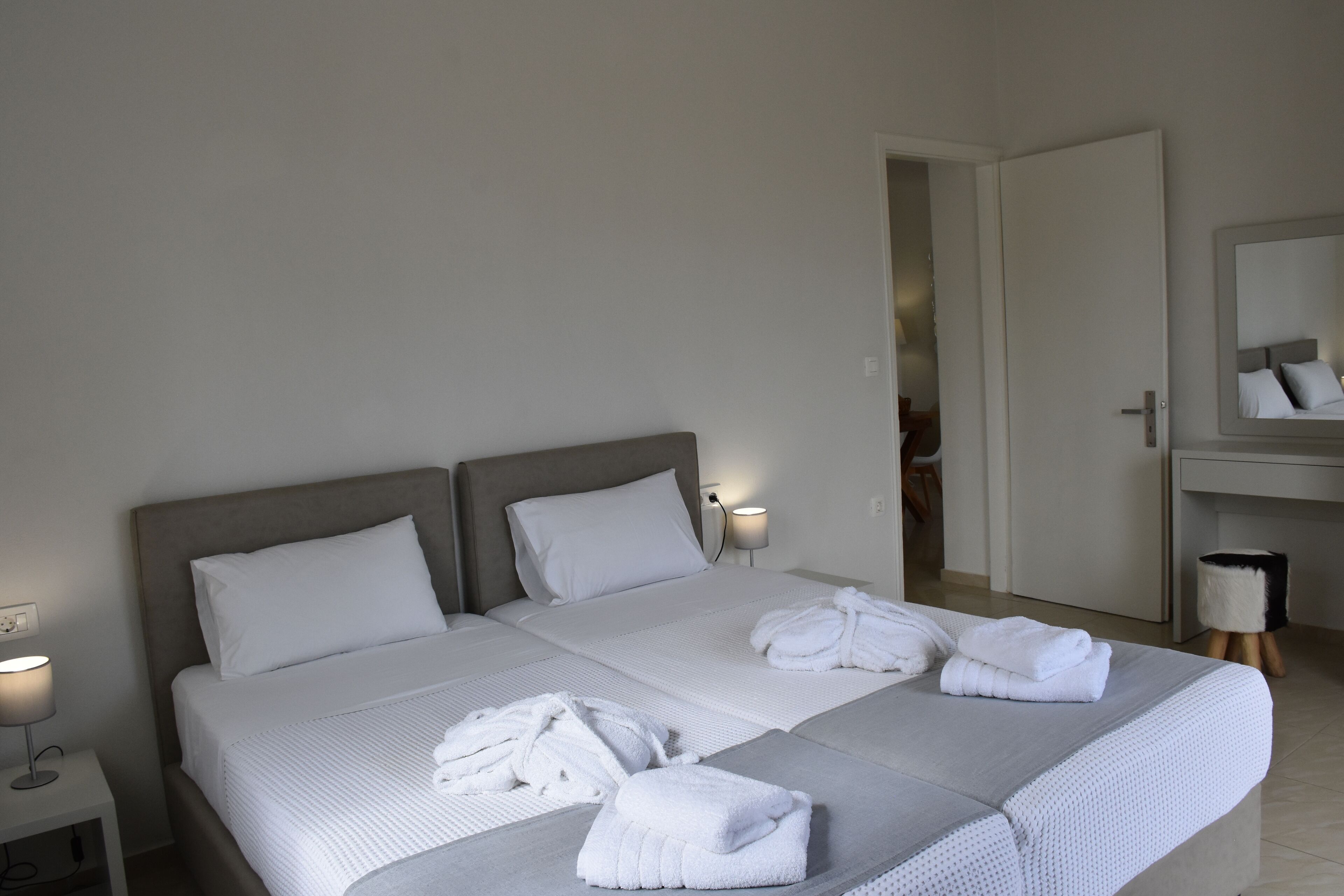Ein Doppelbett mit weißen Bettwäsche und zwei Kissen, ein Nachttisch mit Lampe und ein Spiegel über dem Bett.