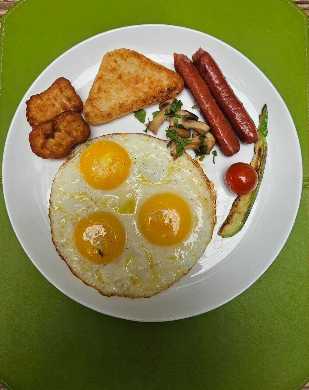 A plate with fried eggs, sausages, and vegetables.