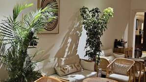 Un área de descanso moderna con mobiliario de mimbre, una planta grande en maceta y una obra de arte colgada en la pared.