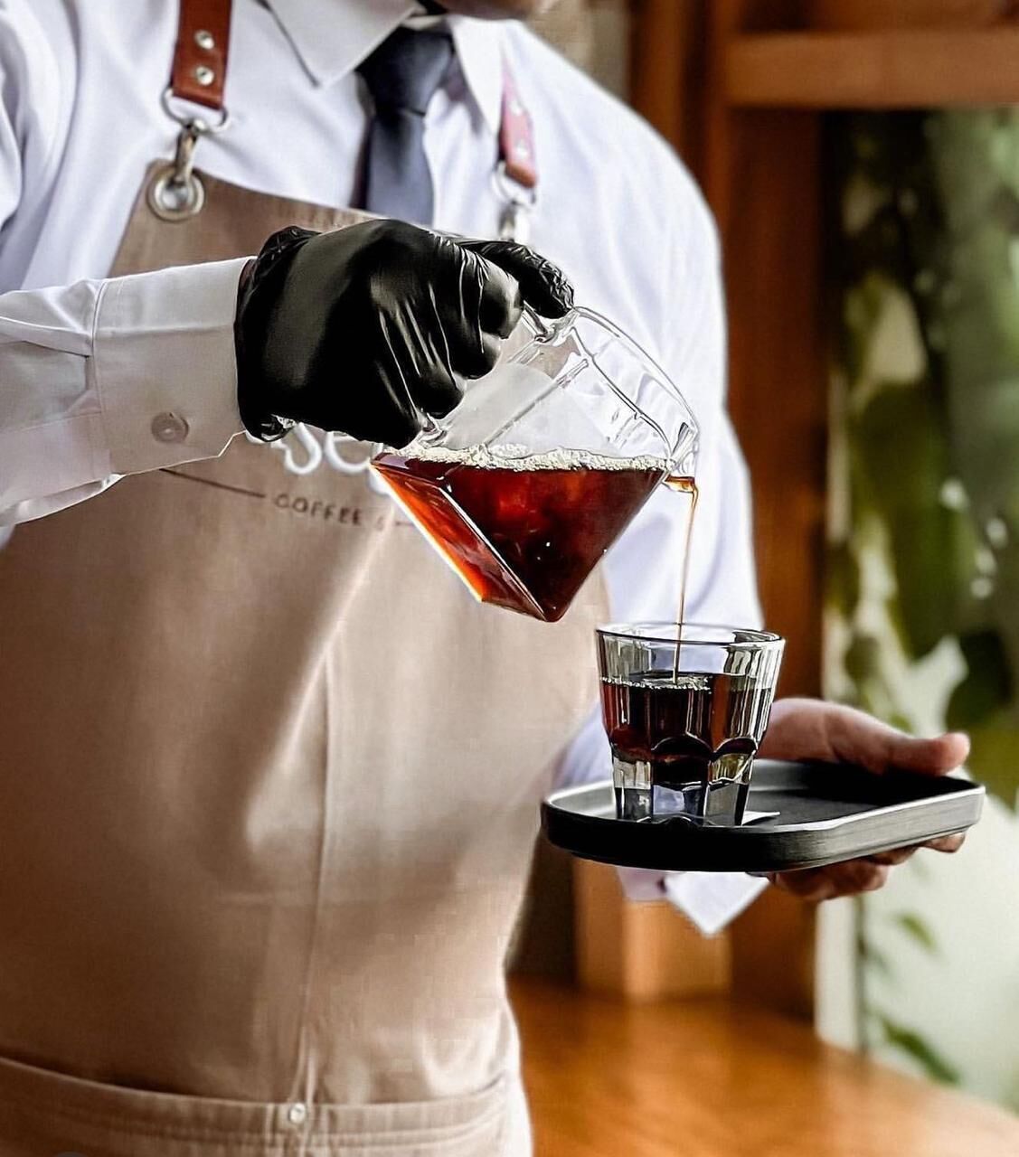 Una persona con camisa y delantal vertiendo una bebida en un vaso.