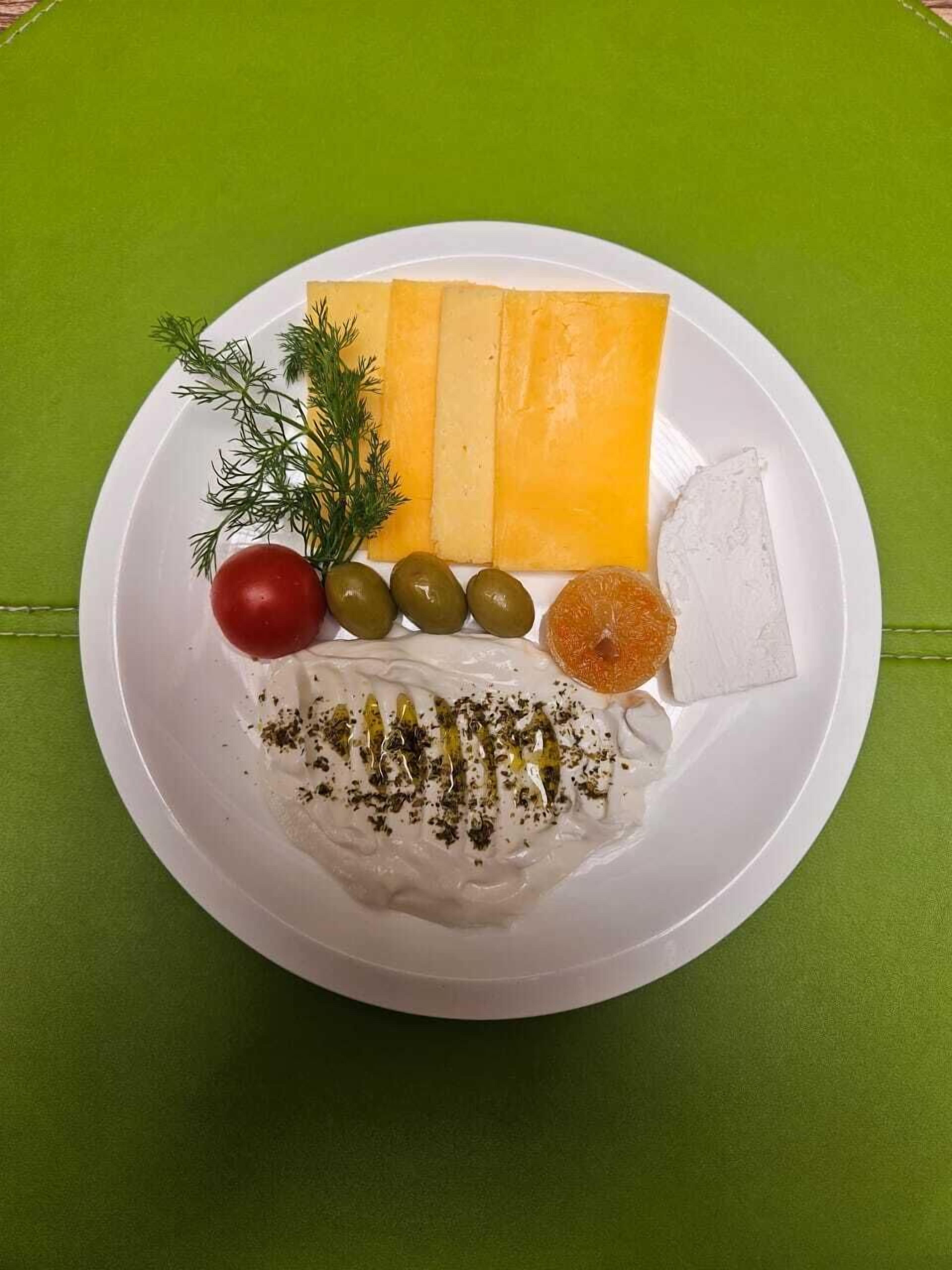 A plate with cheese, olives, a cherry tomato, a sprig of dill, and a dollop of cream with herbs.