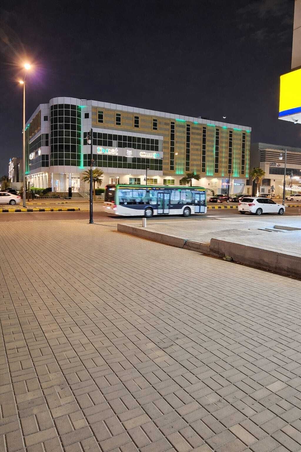 Un edificio moderno con facciata in vetro, un autobus di fronte e un'area pavimentata.