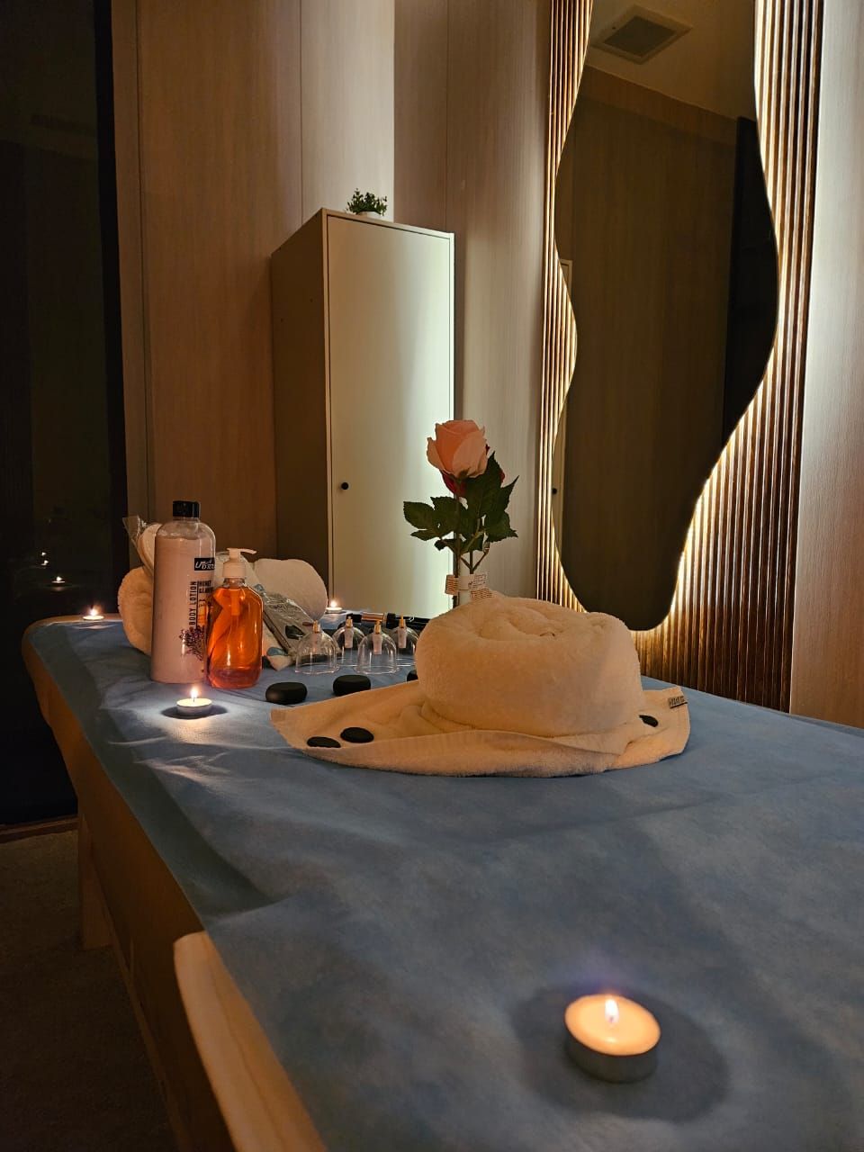 A massage table with candles, a rose, and bottles of lotion.