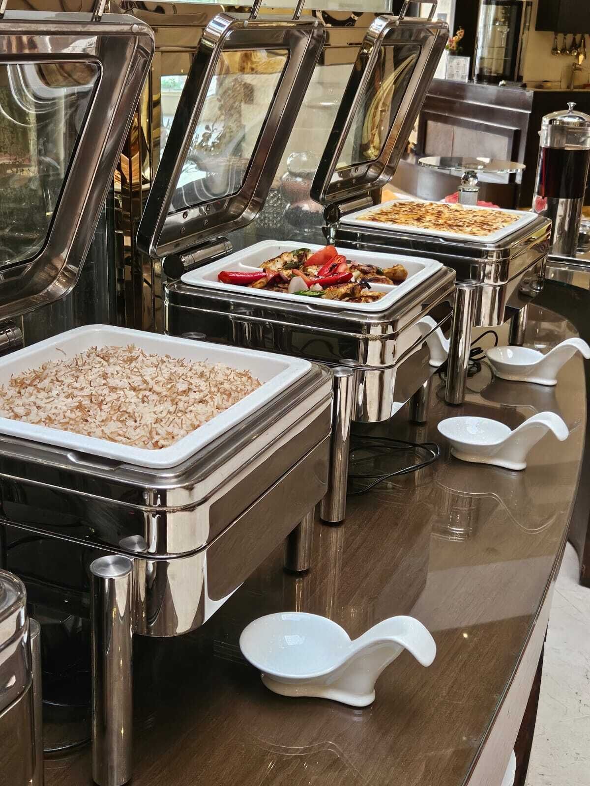 En buffetopstilling med flere serveringsstationer, hver med en overdækket madbeholder og en hvid serverske.