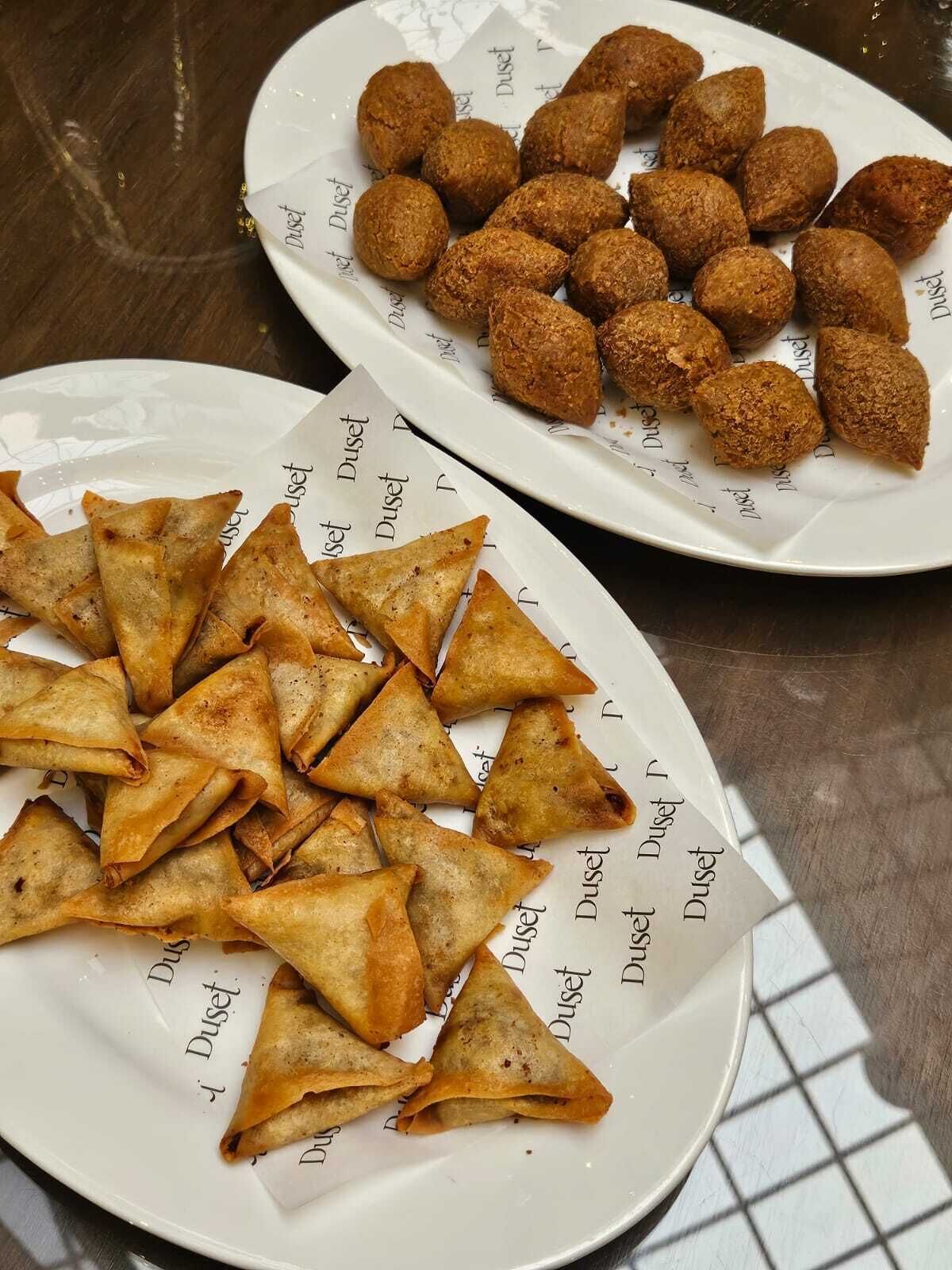 A table with plates of samosas and fried balls.