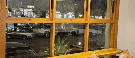 Un banco de madera con sillas acolchadas al frente, un ventanal con múltiples vidrios y lámparas colgantes.