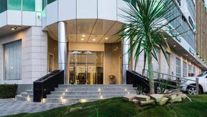 Una entrada de hotel moderna con fachada de vidrio, una escalera que lleva al vestíbulo y una palmera en primer plano.