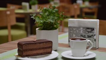 A slice of chocolate cake on a plate, a white cup of coffee, and a potted plant on a table.