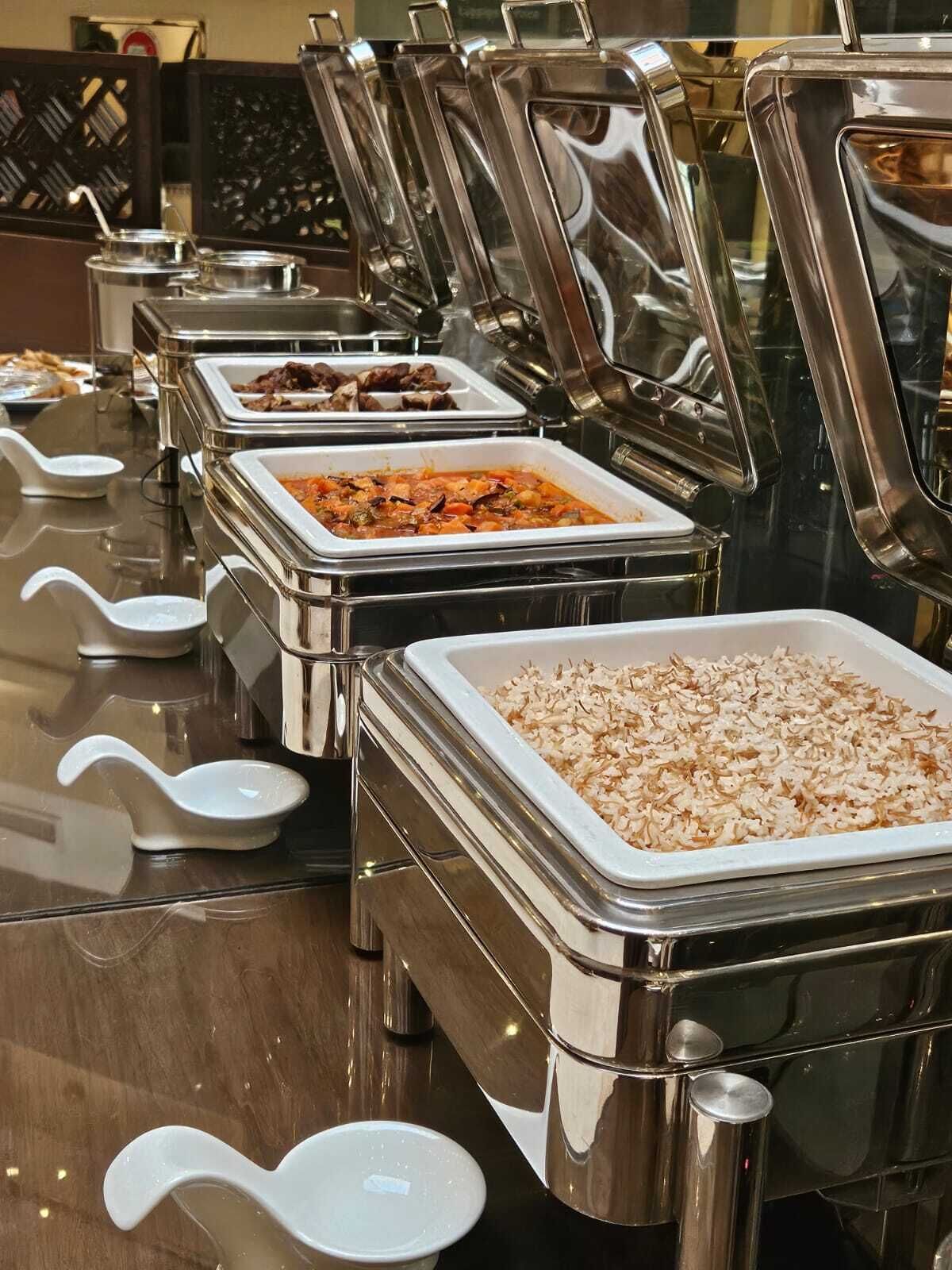 Un buffet con diverse postazioni gastronomiche, ognuna con un mestolo e coperta da un coperchio metallico.