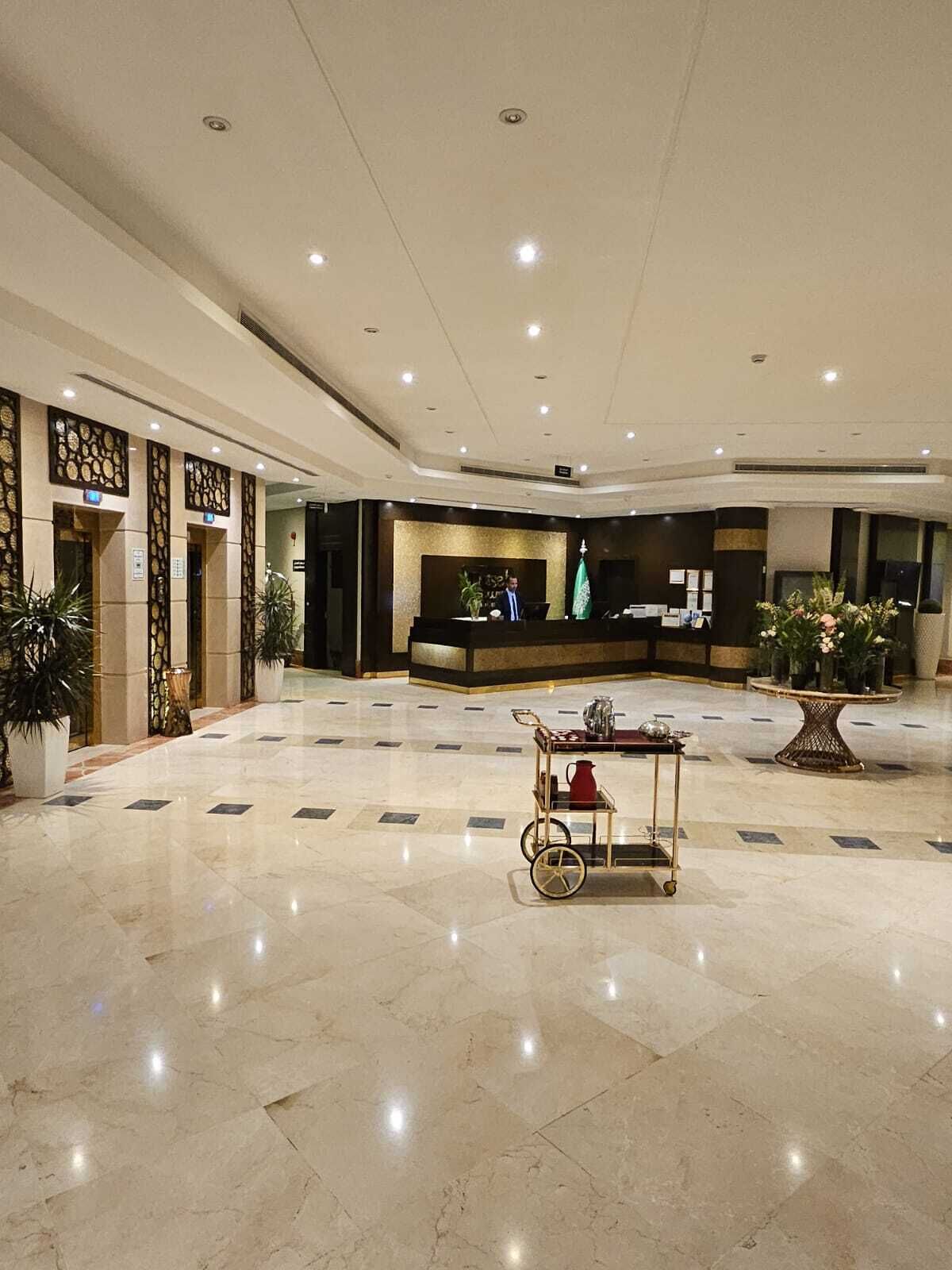 A spacious lobby with a reception desk, potted plants, and a coffee cart.