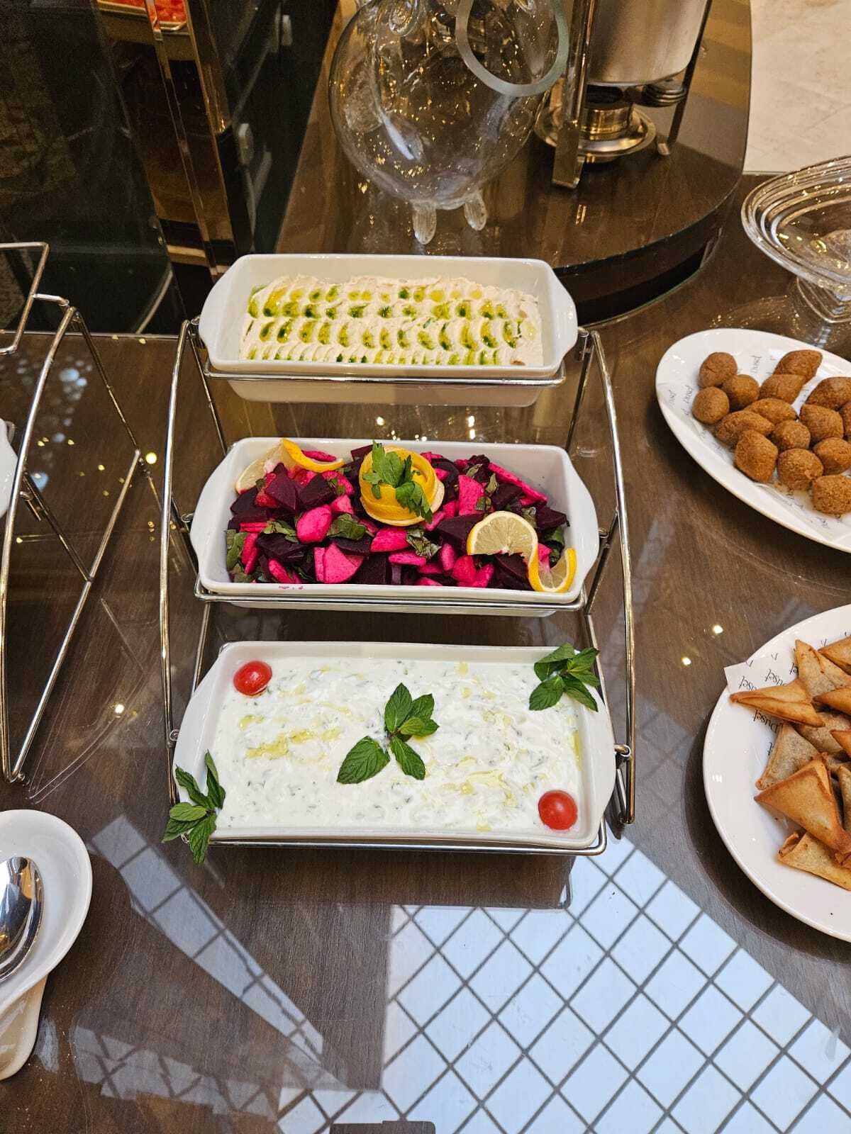 Ein Tisch mit verschiedenen Speisen, darunter eine Schale mit geschnittenem Gemüse, ein Salat mit Rote Bete und Zitrone sowie ein Gericht mit cremiger Sauce, verziert mit Minze.