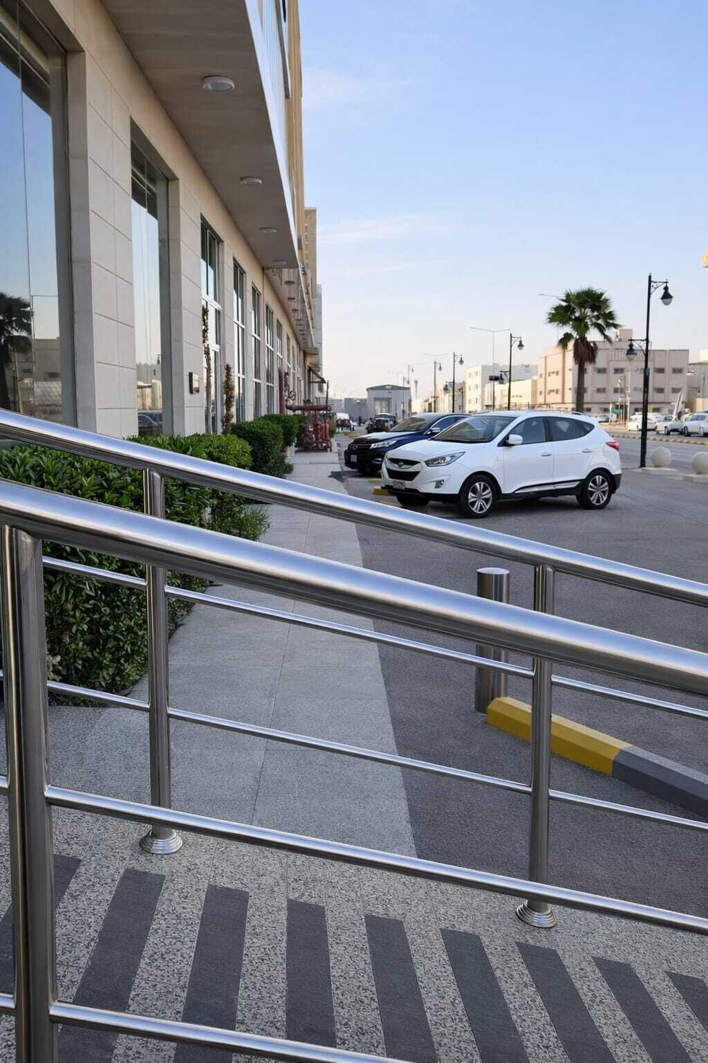 A modern building with a glass facade, a parking area with cars, and a metal staircase leading to the entrance.