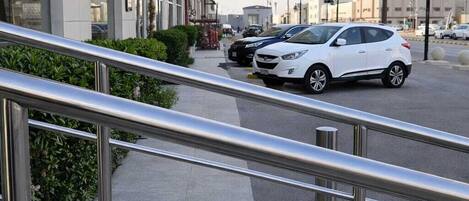 A modern building with a glass facade, a parking area with cars, and a metal staircase leading to the entrance.