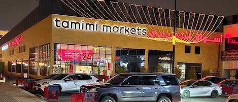 Kauppakeskus, jossa on myymälä nimeltä »Tamimi Markets» ja useita parkkeerattuja autoja.