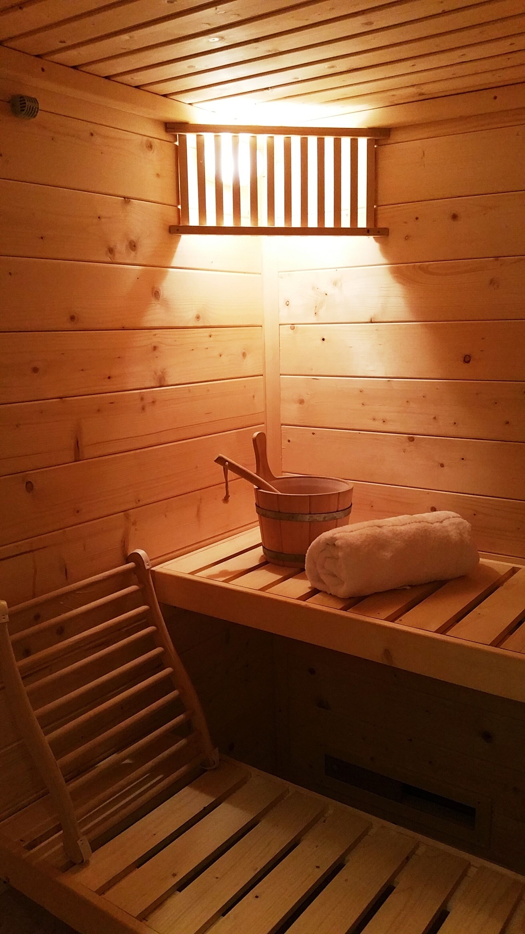Una sauna de madera con un banco, un balde y una toalla.