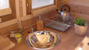 Un intérieur en bois comprenant un coin cuisine avec un évier, une bouilloire, un égouttoir et une plante en pot.