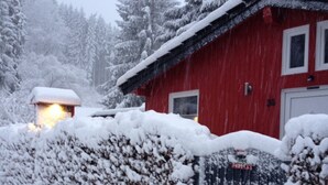 Ein rotes Gebäude mit einem mit Schnee bedeckten Dach und einem schwarzen Zaun.