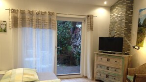 Ein Schlafzimmer mit Bett, Kommode, Fernseher und Blick auf einen Garten durch eine Schiebetür.