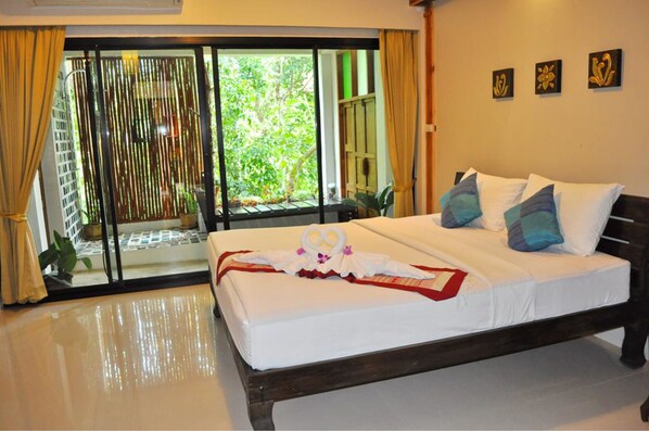 A hotel room with a bed, a view through a sliding door, and a small balcony. - Oopkaew Resort (Pua)