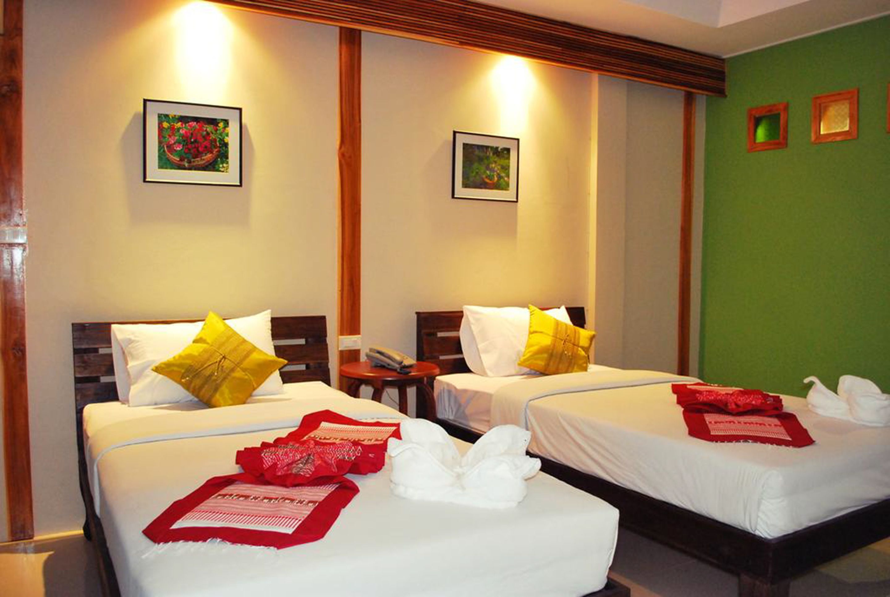 Habitación de hotel con dos camas, cada una con ropa de cama blanca y almohadas amarillas. Se observan cuadros en las paredes, un cabecero de madera y una pared de acento verde.
