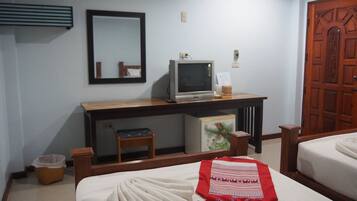 A hotel room with a bed, a desk with a computer, a mirror, and a wooden door.