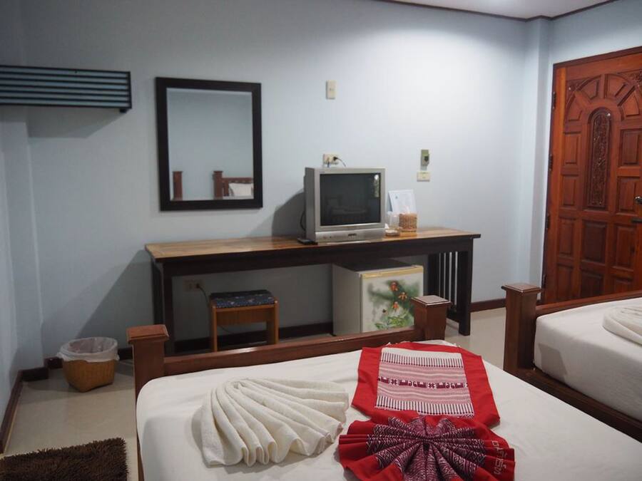A hotel room with a bed, a desk with a computer, a mirror, and a wooden door.