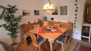 Un comedor con una mesa de madera, sillas y una lámpara colgante. Hay una planta en maceta y obras de arte en las paredes.