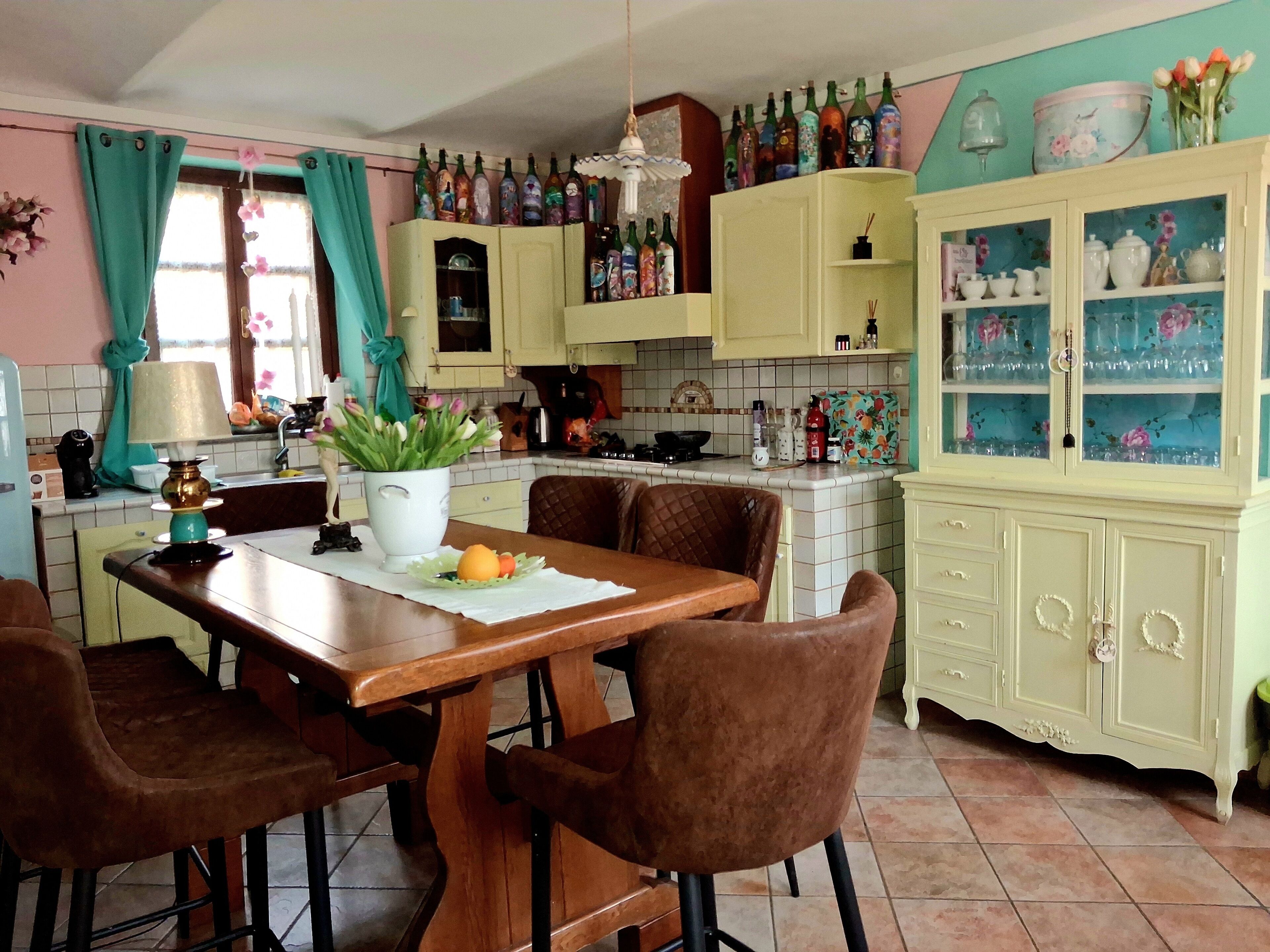 Una cocina con una mesa de madera, sillas, una planta en maceta y un armario con puertas de cristal.