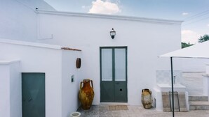 Un edificio blanco con una puerta verde, un aplique de pared y dos grandes jarrones.