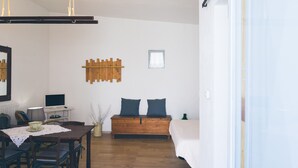 Una habitación con una mesa de comedor de madera, sillas, un sofá con cojines, un ventanal pequeño y un estante montado en la pared.