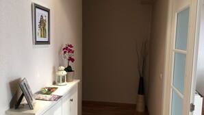 A hallway with a white dresser, a framed picture, a potted orchid, a white lantern, and a vase with branches. - Calle Guerrilleros, entre centro histórico y la zona del Corte Inglès (salamanca)