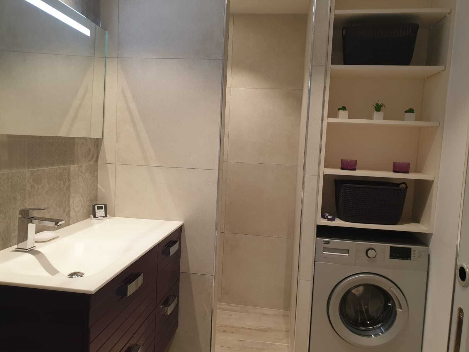 Une salle de bain moderne équipée d’un lavabo, d’un miroir et d’un lave-linge encastré.