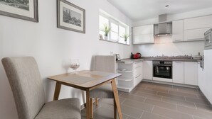 A modern kitchen with white cabinets, a wooden table, and two chairs. There are framed pictures on the wall and a window with plants on the counter. - Sunny days in our dreamlike, beautiful Dresden! (Center) (Dresden)