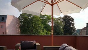 A rooftop terrace with wicker furniture, a white umbrella, and a vase of pink flowers. - Sunny days in our dreamlike, beautiful Dresden! (Center) (Dresden)