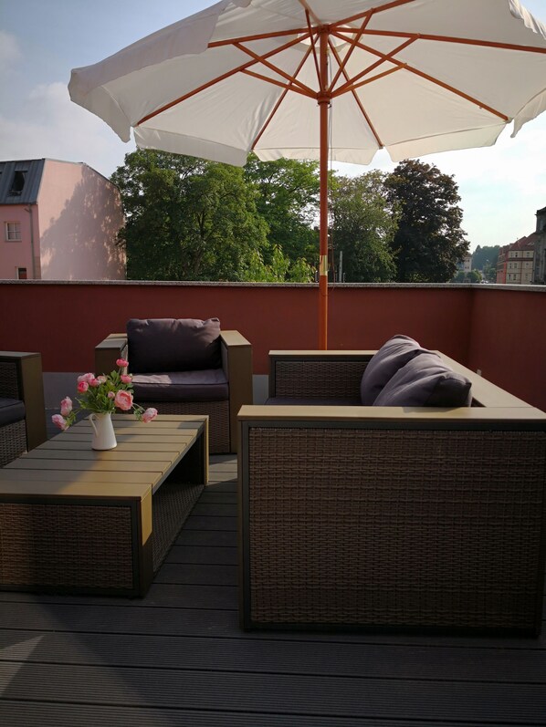 A rooftop terrace with wicker furniture, a white umbrella, and a vase of pink flowers. - Sunny days in our dreamlike, beautiful Dresden! (Center) (Dresden)