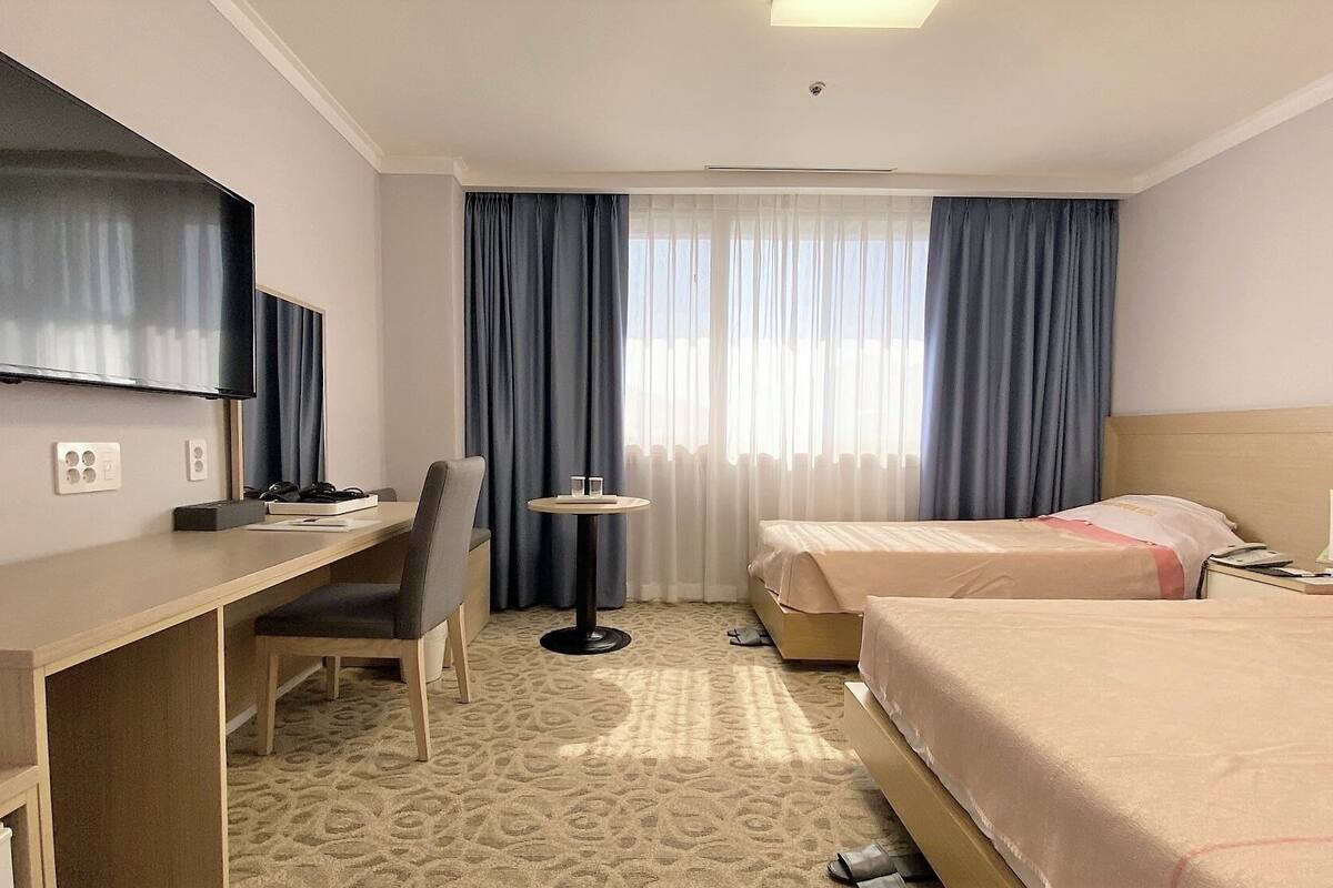 Een hotelkamer met een bureau, twee bedden, een televisie en een klein tafeltje.