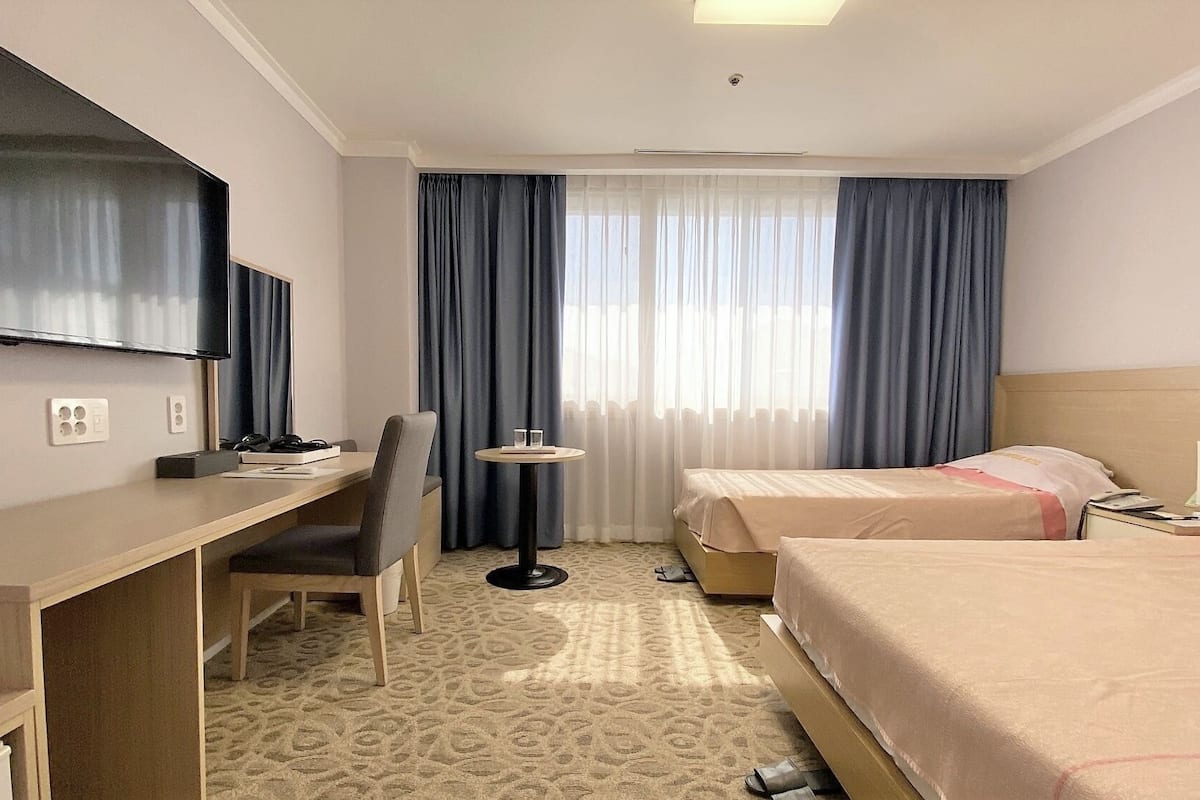 Een hotelkamer met een bureau, twee bedden, een televisie en een klein tafeltje.