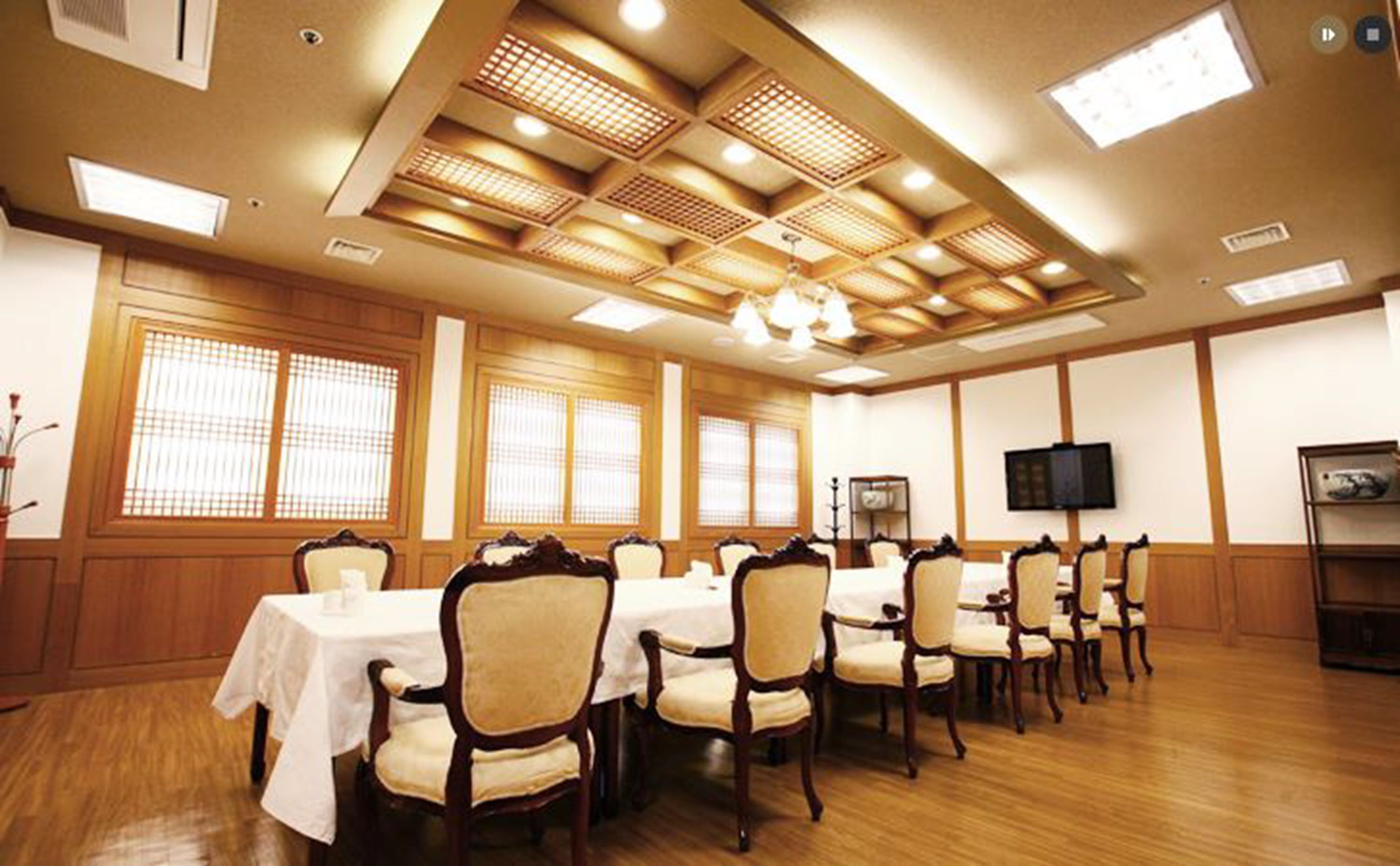 Un salón de conferencias con paneles de madera, una mesa cubierta con mantel blanco y un televisor en la pared.