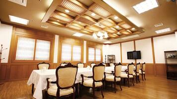 Un salón de conferencias con paneles de madera, una mesa cubierta con mantel blanco y un televisor en la pared.