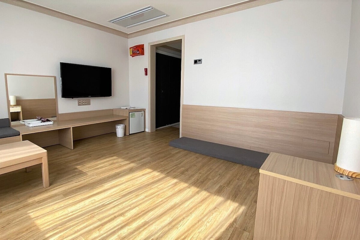 Een hotelkamer met een bed, een bureau, een televisie, een kleine koelkast en een prullenbak.