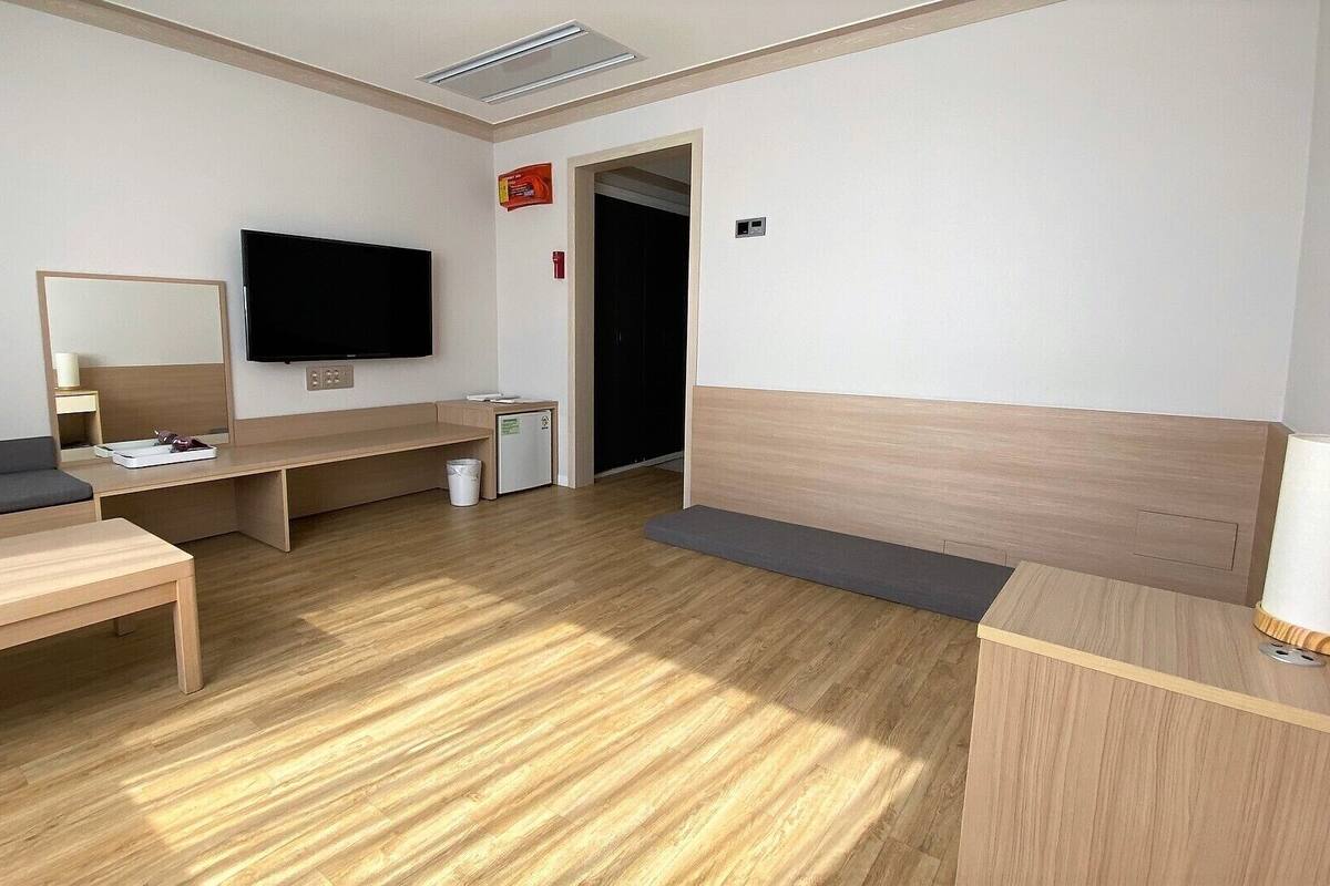 Een moderne hotelkamer met een houten vloer, een bank, een bureau, een televisie en een kleine koelkast.