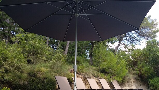 Un espace piscine doté d’un grand parasol, de chaises longues et d’une bordure en béton.